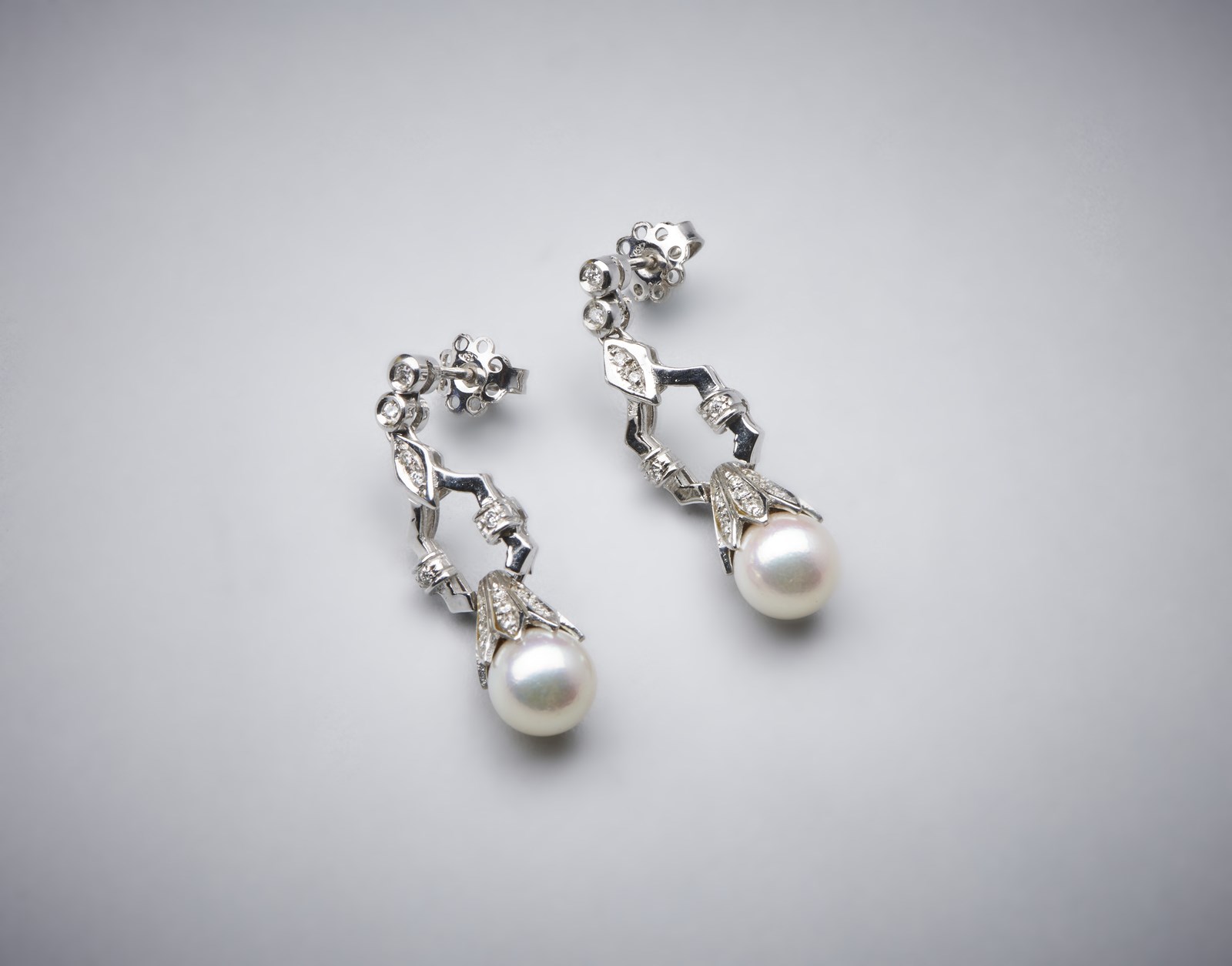 Orecchini pendenti in oro bianco 750/1000 con coppia di perle sferiche bianche coltivate di mm 8,50 e piccoli diamanti bianchi di taglio misto di 0,80 ct circa. (. )