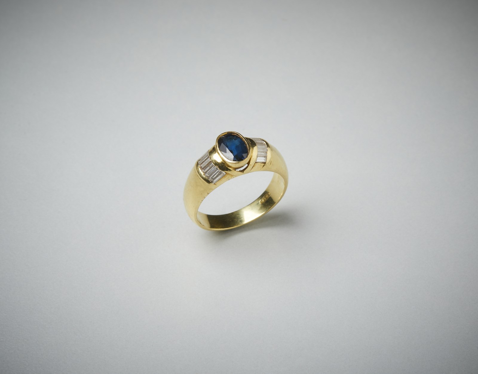 Anello in oro giallo 750/1000  a fascetta con zaffiro blu ovale di 0.70  ct ca. e diamanti bianchi laterali taglio a baguette di 0.75 ct totali circa.   (. )