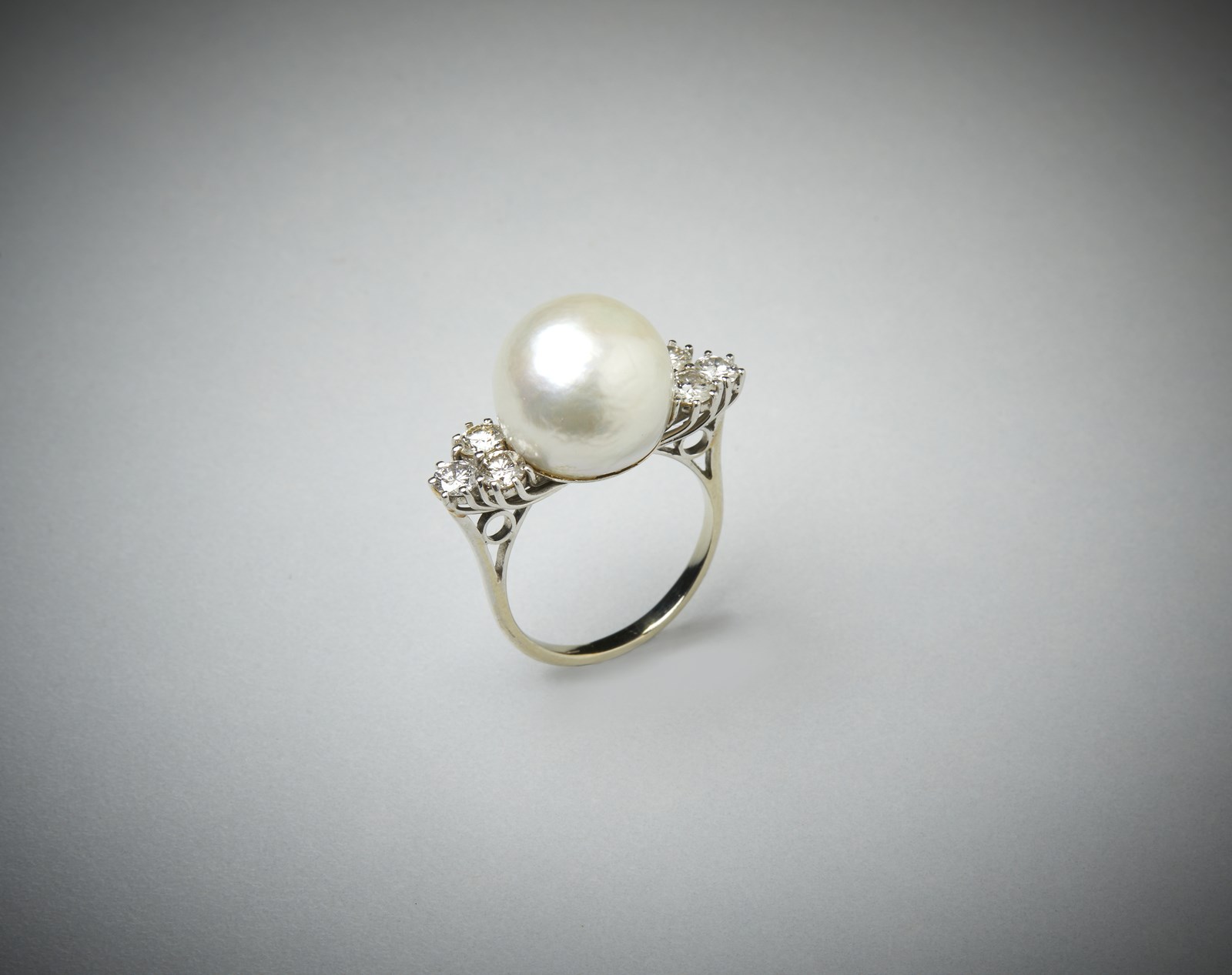 Anello con perla  bianca coltivata e sei diamanti laterali taglio a brillante di circa 1 ct. totale. (. )